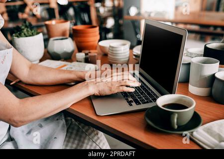 Eine letzte Anpassung an meinen Zeitplan. Eine unkenntliche Frau sitzt und benutzt ihren Laptop in ihrer Töpferwerkstatt. Stockfoto