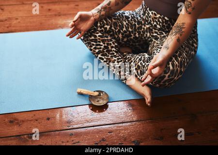 Reinigung des Raumes um sie herum, um tiefe Entspannung zu fördern. Nahaufnahme einer Frau, die einen palo santo-Stick verbrennt, während sie zu Hause auf einer Yogamatte meditiert. Stockfoto