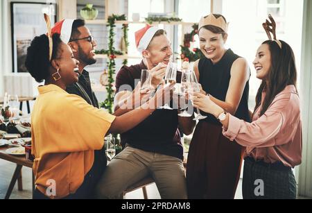 Es ist die glücklichste Jahreszeit überhaupt. Eine Gruppe von fröhlichen jungen Freunden, die anstoßen, während sie Weihnachten gemeinsam zu Hause feiern. Stockfoto