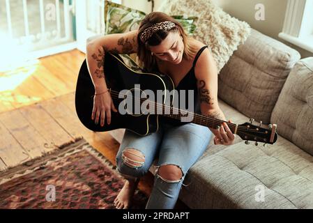 Ich bin mehr mit einer Gitarre in den Händen. Eine junge Frau, die an einem entspannten Tag zu Hause Gitarre spielt. Stockfoto