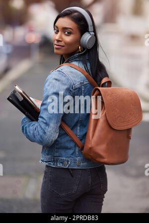 Sie müssen heute mit Ihrer Zukunft beginnen: Eine junge Frau, die mit Kopfhörern durch die Stadt geht und ihre Bücher trägt. Stockfoto