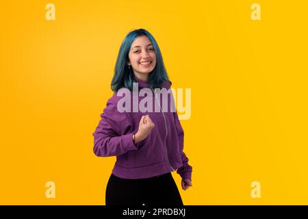 Süßer junger Gilr mit blauem Haar, der eine Siegergeste macht, feiert knallende Fäuste. Isoliert auf einem Studio-Porträt mit gelbem Hintergrund. Stockfoto