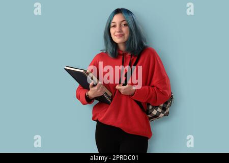 Süße junge Gilr-Schülerin mit blauen Haarbüchern und einem Rucksack Stockfoto