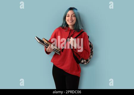 Süße junge Gilr-Schülerin mit blauen Haarbüchern und einem Rucksack Stockfoto