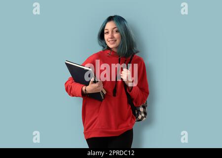 Süße junge Gilr-Schülerin mit blauen Haarbüchern und einem Rucksack Stockfoto