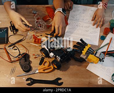 Es ist an der Zeit, dieses Kunstwerk zusammenzubauen. Zwei nicht erkennbare junge Geschwister bauen zu Hause zusammen ein Roboterspielzeug. Stockfoto