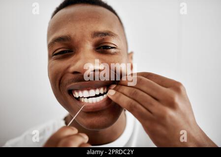 Zahnseide für sauberere, gesündere Zähne. Ein junger Mann, der zu Hause im Badezimmer seine Zähne mit Zahnseide ausgibt. Stockfoto