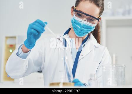 Ich muss das sehr sorgfältig anzeigen. Eine nicht erkennbare junge Wissenschaftlerin, die Gesichtsschutz trägt, während sie Experimente in einem Labor durchführt. Stockfoto