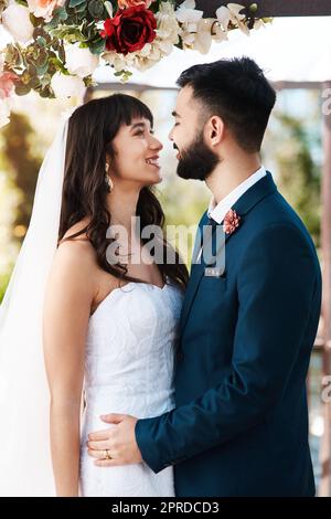 Du bist meine fehlende Rippe. Ein liebevolles junges Paar, das sich gegenseitig anlächelt, während es an ihrem Hochzeitstag draußen steht. Stockfoto