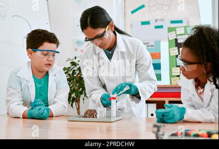 In der heutigen Klasse geht es um chemische Reaktionen. Ein entzückendes kleines Mädchen und ein Junge führen ein wissenschaftliches Experiment mit ihrem Lehrer in der Schule durch. Stockfoto