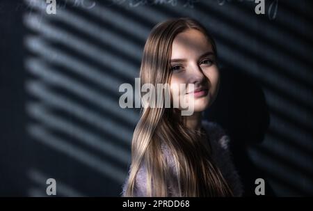 Hübsche, junge Schülerin vor einer Tafel während der Klasse Stockfoto