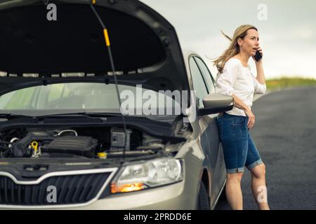 Ziemlich Frau mittleren Alters, die Autoprobleme hat - zusammengebrochenes Auto auf der Seite der Straße, die Versicherungsgesellschaft um Hilfe zu rufen Stockfoto