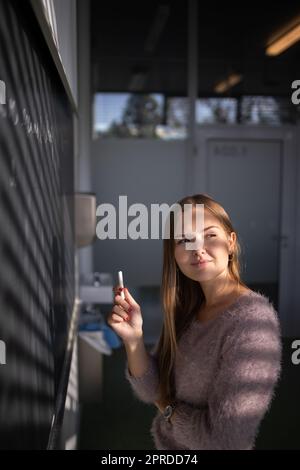 Hübsche, junge Schülerin vor einer Tafel während der Klasse Stockfoto