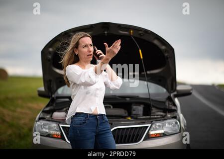 Ziemlich Frau mittleren Alters, die Autoprobleme hat - zusammengebrochenes Auto auf der Seite der Straße, die Versicherungsgesellschaft um Hilfe zu rufen Stockfoto