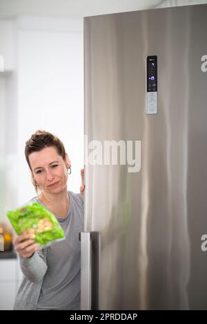 Hübsche, junge Frau, die Lebensmittel aus dem Kühlschrank nehmen, Kontrolle der Termine, gesunde Ernährung Konzept, Haushalt lifestyle Konzept Stockfoto