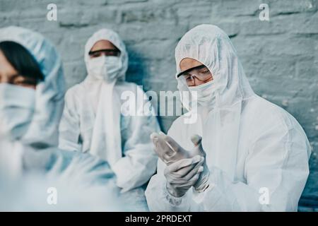 Covid-, Pandemie- und Team-Mitarbeiter im Gesundheitswesen tragen schützende psa, um die Ausbreitung des Virus an einer Quarantänestelle zu verhindern. Besorgter Ersthelfer trägt einen Schutzanzug und überprüft seinen Schutzhandschuh Stockfoto