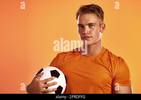 Wir sehen uns auf dem Feld. Studioporträt eines hübschen jungen Fußballspielers, der vor einem orangefarbenen Hintergrund posiert. Stockfoto