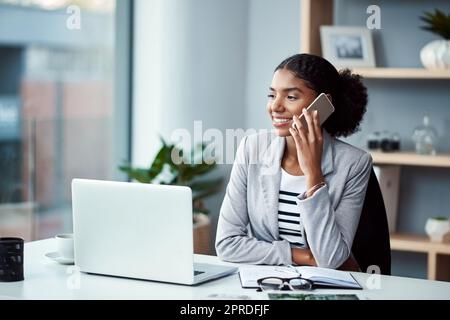 Geschäftsfrau, die telefoniert, oder junger Unternehmer, der vor dem Laptop im Büro das Handy entgegennimmt. Glückliche afroamerikanische Frau, die lächelt und gute Nachrichten erhält, während sie am Schreibtisch sitzt. Stockfoto