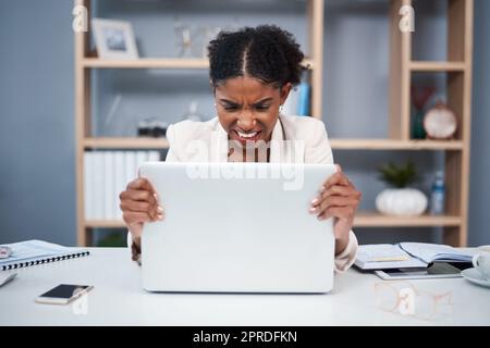 Frustrierte, verärgerte und gestresste junge Geschäftsfrau mit einem Notebook in einem modernen Büro. Frau zeigt am Arbeitsplatz Wut mit Technologie. Eine Mitarbeiterin greift sich den Computer an, weil die Verbindung langsam ist Stockfoto