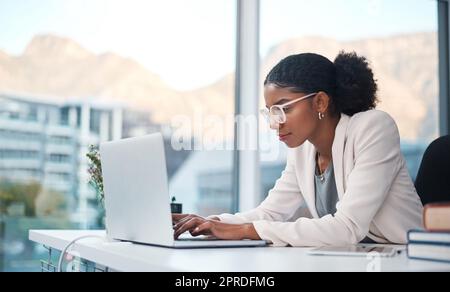 Datenexperte und Sekretärin, die eine E-Mail auf einem Laptop schreibt und online recherchiert, während sie in einem Büro arbeiten. Afrikanischer Unternehmer, der fokussiert ist, während er das Internet für die Arbeit nutzt Stockfoto