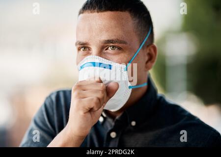 Ein junger Mann hustet und trägt eine Maske vor einem Stadthintergrund. Stockfoto