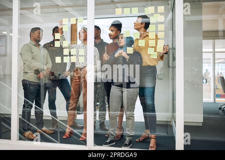 Planen Sie gut, damit Sie großen Erfolg haben können. Eine Gruppe von Geschäftsleuten Brainstorming mit Notizen an einer Glaswand in einem Büro. Stockfoto