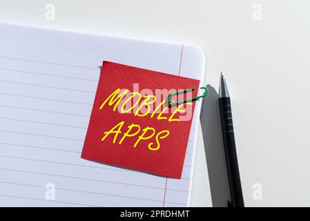 Konzeptionelle Darstellung von mobilen Apps. Word for Small Programme funktionieren auf Telefonen wie dem App Store oder dem App Store Sticky Note mit einer wichtigen Idee, die auf einem geöffneten Notebook auf dem Schreibtisch mit Stift befestigt ist Stockfoto