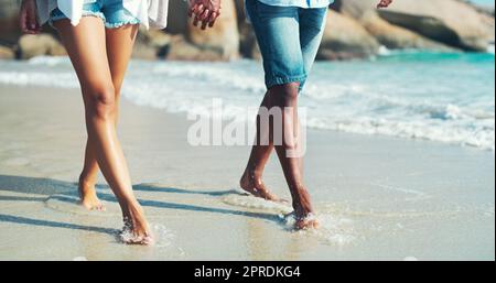 Der Lauf der wahren Liebe ist ein Strandspaziergang. Ein unerkennbares, liebevolles Paar, das am Strand spazieren geht. Stockfoto