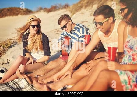 Hes die Art von Freund, der Ihnen ein Lied spielen wird. Ein hübscher junger Mann, der an einem Sommertag am Strand eine Gitarre für seine Freunde spielt. Stockfoto