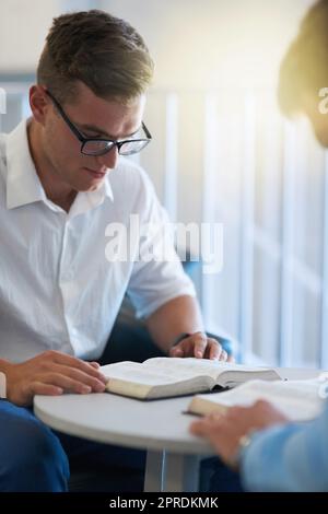 Zwei junge Geschäftsleute, die ihre Bibeln bei der Arbeit lasen, suchten nach einer göttlichen Intervention. Stockfoto