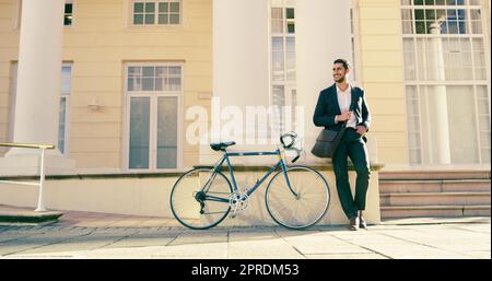 Er wird heute seinen positiven Geist im ganzen Büro verbreiten. Ein Foto eines gutaussehenden jungen Geschäftsmannes, der sich neben einem Fahrrad in der Stadt posiert. Stockfoto