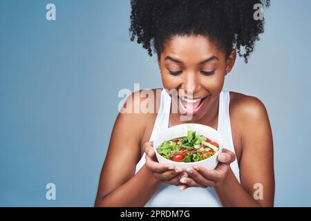 Es sieht toll aus und schmeckt noch besser. Studioaufnahme einer attraktiven jungen Frau, die vor grauem Hintergrund Salat isst. Stockfoto