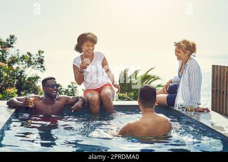 Ein paar Freunde, die im Urlaub am Pool etwas trinken und sich amüsieren, beenden ihr Jahr mit einem Spritzer. Stockfoto