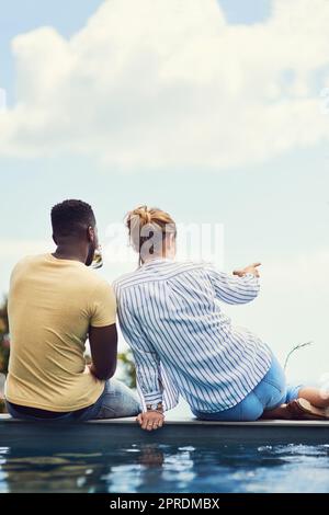 Anscheinend gibt es dort ein Einkaufszentrum. Rückansicht eines jungen Paares, das zusammen Getränke genießt und sich im Urlaub im Freien entspannt. Stockfoto