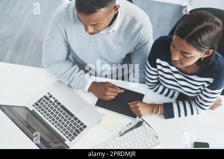 Seien Sie immer bereit, im Geschäft zu lernen und zu versuchen. Aufnahme von zwei jungen Geschäftsleuten, die auf einem Laptop an ihrem Schreibtisch durch Figuren gehen. Stockfoto