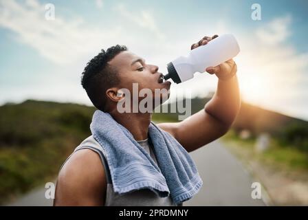 Abkühlung nach einem intensiven Lauf. Ein sportlicher junger Mann trinkt beim Training im Freien Wasser. Stockfoto