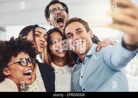 Teamwork, spielerisch und Selfie, während eine Gruppe fröhlicher Geschäftsleute für einen Beitrag in sozialen Medien lustige Gesichter kreiert. Gesichter eines glücklichen und lustigen Teams, das in einem kreativen Büro zusammensteht Stockfoto