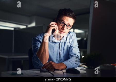 Gestresst, überarbeitet und besorgt, als ich telefonierte, um Probleme zu lösen, während ich spät nachts im Büro arbeite. Ein ernster und erschöpfter Mann, der wegen Computerproblemen anruft und versucht, die Frist zu erreichen Stockfoto