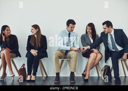 Verbinden Sie sich mit geschäftsorientierten Menschen. Studio-Aufnahme einer Gruppe von Geschäftsleuten, die drahtlose Technologie nutzen, während sie in der Schlange warten. Stockfoto