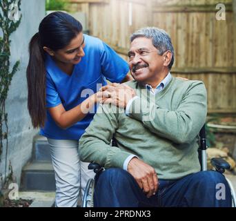 Danke, dass du dich immer um mich kümmerst. Ein fröhlicher älterer Mann sitzt im Rollstuhl, während er tagsüber von einer Krankenschwester draußen zu Hause unterstützt wird. Stockfoto