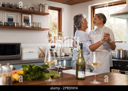 Verlieben Sie sich wieder. Ein glückliches reifes Paar tanzt zusammen, während es in der Küche zu Hause kocht. Stockfoto