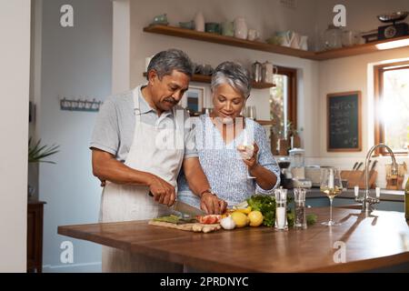 Was machen Sie, Honig. Ein glückliches reifes Paar Wein trinken, während eine Mahlzeit zusammen zu Hause kochen. Stockfoto