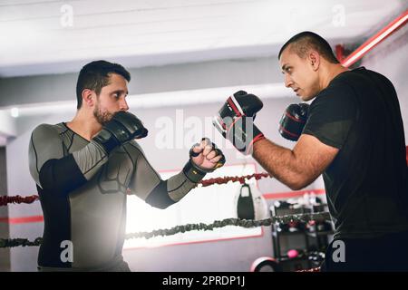 Zwei junge Boxer, die sich tagsüber in einem Trainingskampf in einem Boxring in einer Turnhalle gegenüberstehen, stehen sich gegenüber. Stockfoto