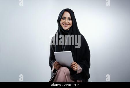 Ein Unternehmer zu sein, passt zu meinem Lebensstil. Abgeschnittenes Porträt einer attraktiven jungen Geschäftsfrau, die ihr Tablet vor grauem Hintergrund verwendet. Stockfoto