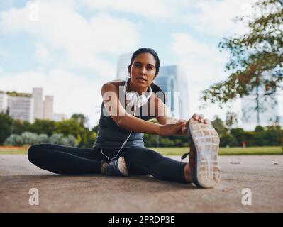 Die Magie liegt im Aufwärmen. Ganzkörperaufnahme einer attraktiven jungen Sportlerin, die im Freien Stretchübungen in der Stadt macht. Stockfoto