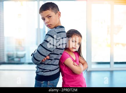 Sie haben nichts Gutes zu bringen. Portrait von zwei frechen kleinen Kindern, die mit gefalteten Armen und Rücken zu Hause posieren. Stockfoto