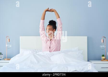 Ich fühle mich erfrischt und bereit, die Welt zu übernehmen. Eine attraktive junge Frau posiert mit ihren Armen im Bett zu Hause angehoben. Stockfoto