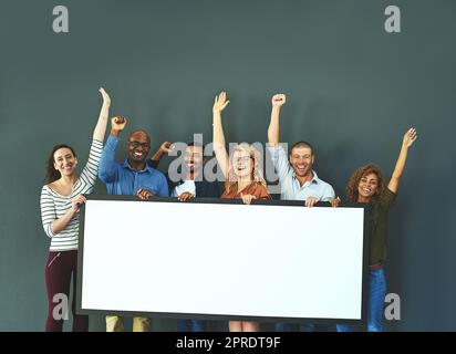 Aufgeregte Geschäftsleute, die ein leeres Schild zeigen, ein Produkt bewerben und eine Botschaft auf einer Tafel vermitteln, während sie zusammen in einem Büro bei der Arbeit stehen. Porträt glücklicher Kollegen mit leerem Poster Stockfoto