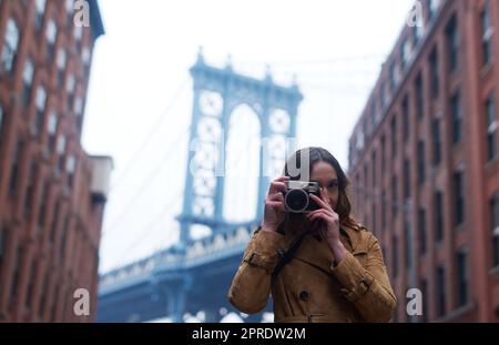 Verpassen Sie keinen einzigen Speicher mehr. Porträt einer attraktiven jungen Frau, die mit einer Kamera in der Stadt fotografiert. Stockfoto