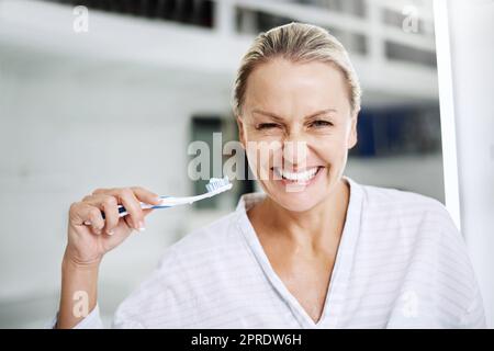 Je mehr man bürstet, desto weißer werden sie. Eine reife Frau posiert mit einer Zahnbürste. Stockfoto